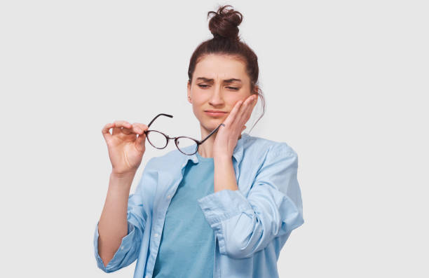 istock Questioned pretty young woman has thinking expression, looking through her transparent eyeglasses. Doubtful girl wears eyewear can`t make choice, has questioned expression, on white wall 1164295110