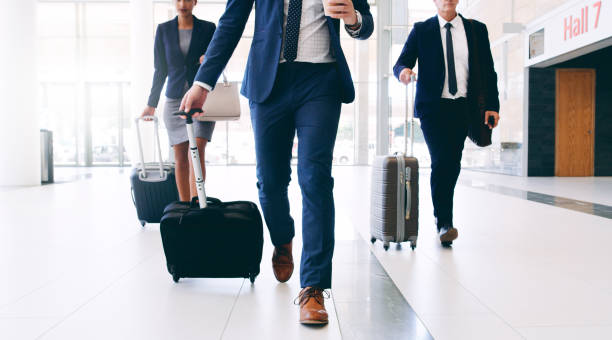Our business requires us to travel Cropped shot of three unrecognizable businesspeople walking and pulling suitcases while in the office during the day business travel stock pictures, royalty-free photos & images
