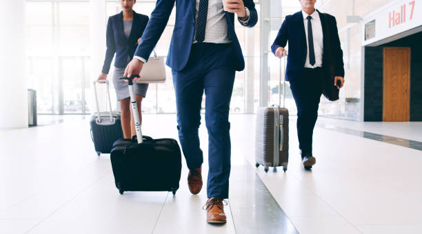 Our business requires us to travel Cropped shot of three unrecognizable businesspeople walking and pulling suitcases while in the office during the day business journey stock pictures, royalty-free photos & images
