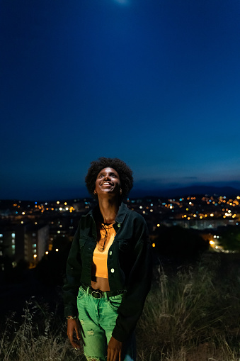 Young woman looking up with hope. Shot at twilight, with the city lights at background.