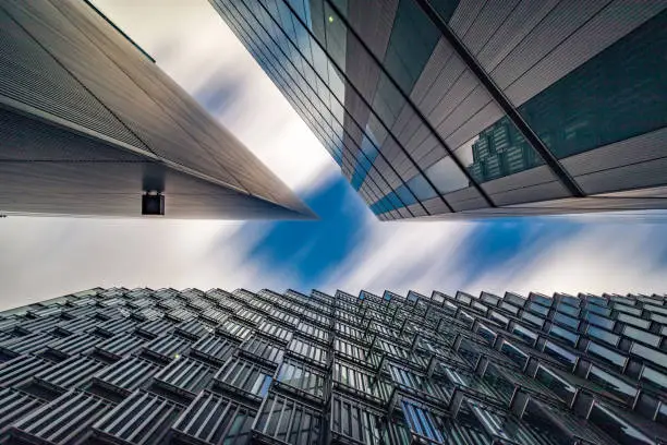Highly detailed abstract wide angle view up towards the sky in the financial district of London City and its ultra modern contemporary buildings and conceptual shaped architecture. Image is ideal for background with copy space. Shot on Canon EOS full frame system. Long exposure to blur the white clouds on a sunny day, colour image with high contrast.