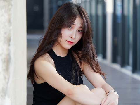 Graceful Young Woman With Long Black Hair Sitting On Ground And Leaning On  The Wall In Sunny Day Outdoor Portrait Of Cool Chinese Girl In Trendy  Summer Sexy Black Dress And Sandals