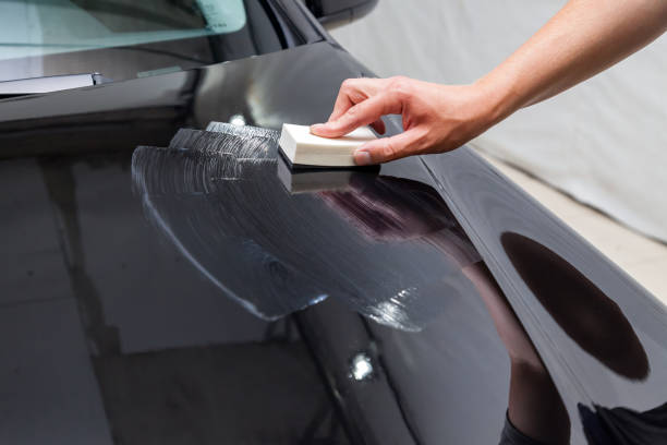 der prozess des auftragens einer nano-keramik-beschichtung auf die motorhaube des autos durch einen männlichen arbeiter mit einem schwamm und einer speziellen chemischen zusammensetzung, um die farbe auf dem körper vor kratzern, spänen und beschädigung - glass car repairing auto repair shop stock-fotos und bilder