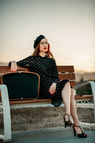 jeune femme dans la robe noire de point de polka de cru avec la valise rétro dans la main posant à l'extérieur - polka dot suitcase retro revival women photos et images de collection