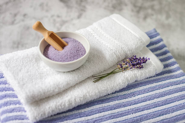 istock Stack of clean soft towels with a bunch of lavender and  bath salt on light gray background. 1164319842