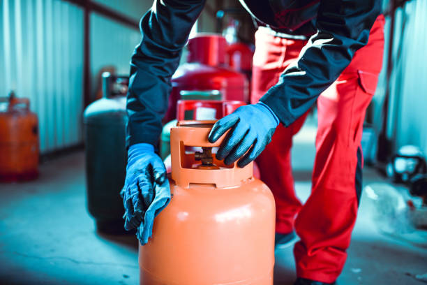 male worker cleaning gas cylinder in storage - botija de gas imagens e fotografias de stock