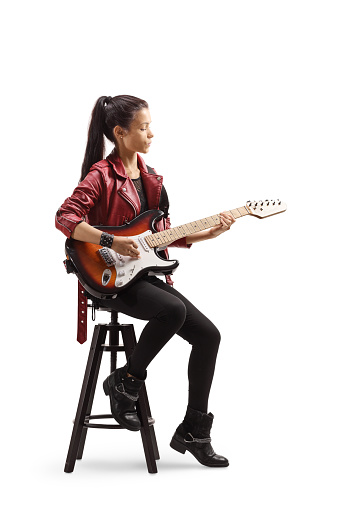 Full length shot of a young female musician sitting on a chair and playing electric guitar isolated on white background