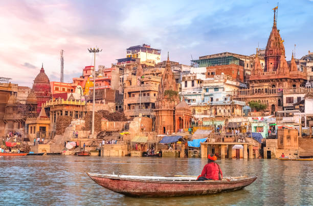 sadhu hindú sentado en un barco con vistas a la arquitectura de la ciudad de varanasi al atardecer - subcontinente indio fotografías e imágenes de stock