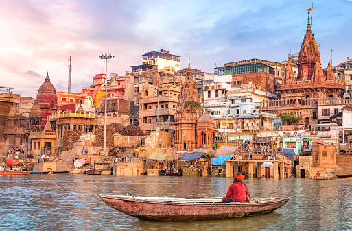 Ancient Varanasi city architecture and Ganges river ghat at sunset with view of an Indian sadhu sitting a boat on the river Ganges.