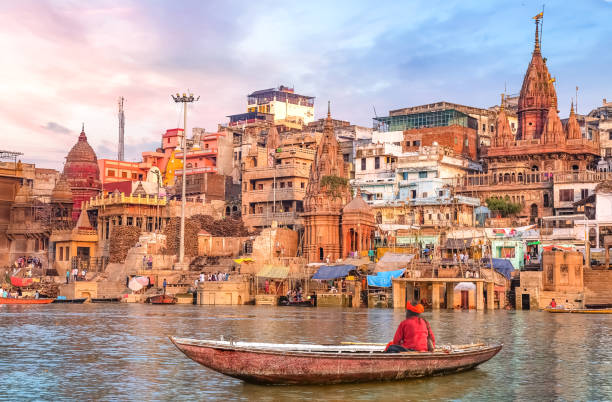 Hindu sadhu sitting on a boat overlooking Varanasi city architecture at sunset Ancient Varanasi city architecture and Ganges river ghat at sunset with view of an Indian sadhu sitting a boat on the river Ganges. monk religious occupation photos stock pictures, royalty-free photos & images