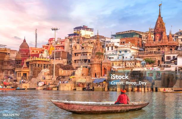 Download Hindu Sadhu Sitting On A Boat Overlooking Varanasi City Architecture At Sunset Stock Photo