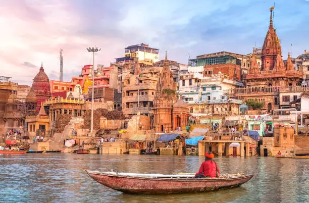 Ancient Varanasi city architecture and Ganges river ghat at sunset with view of an Indian sadhu sitting a boat on the river Ganges.