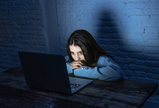 dramatic portrait of sad, scared young woman on laptop suffering cyber bullying and harassment. - sleaze imagens e fotografias de stock