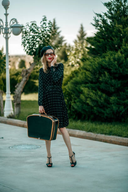 jeune femme dans la robe noire de point de polka de cru avec la valise rétro dans la main posant à l'extérieur - polka dot suitcase retro revival women photos et images de collection