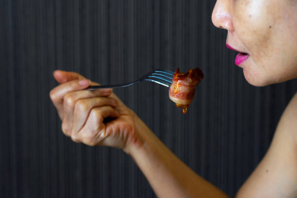 Asian woman holding fork with bacon wrapped sausage and sauce stock photo
