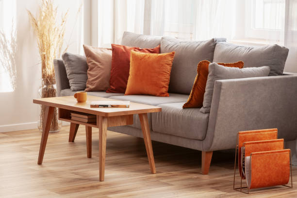 Living room with wooden coffee table and grey couch with ginger, orange and red pillows stock photo