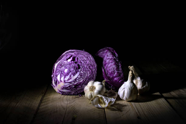 istock Red cabbage halves and ripe garlic in backlight lying on a wooden surface. Still life on a black background. 1164339407