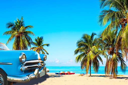The tropical beach of Varadero in Cuba with american classic car, sailboats and palm trees on a summer day with turquoise water. Vacation background