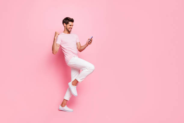 verticale pleine longueur de vue de taille de corps de son il il gentil le gentil le gentil le gentil le gentil le gentil le gentil le gentil le bon gai le gars lisant la notification de bonnes nouvelles se réjouissant d'isolement au-dessus du fond pastel - smart casual cheerful content image photos et images de collection