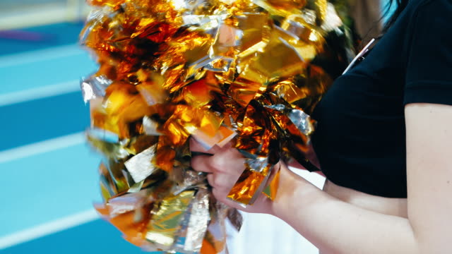 Girl cheerleader holding pompoms during athletics championship. Motley pompoms in hands