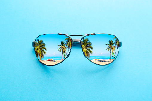 Concepto de vacaciones de verano. Gafas de sol con playa oceánica y palmeras sobre fondo azul. photo