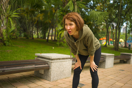 outdoors portrait of young attractive tired and breathless jogger woman in breathing exhausted after running workout at beautiful city park in fitness sport training and healthy lifestyle concept