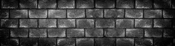 Wide dark concrete brick block wall. Black shabby texture. Panoramic gloomy grunge background