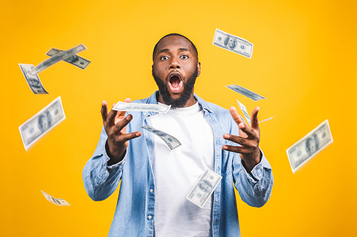 Retrato de un joven feliz hombre afroamericano tirando billetes de dinero aislados sobre fondo amarillo. photo