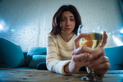 Portrait of depressed woman drinking glass of wine alone at home. Feeling distress, hopeless and frustrated, trying to feel better drinking. Unhealthy behavior, depression and alcohol concept.