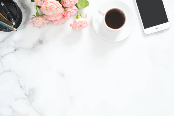istock Flat lay, top view office table desk. Feminine desk workspace frame with coffee cup, floral bouquet, smartphone and stationery on white marble background. 1164372097
