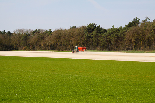 ROERMOND, NETHERLANDS - MARCH 30. 2019: Chalk fertilizer application by tractor with spreader to prepare the field for growing grass lawn