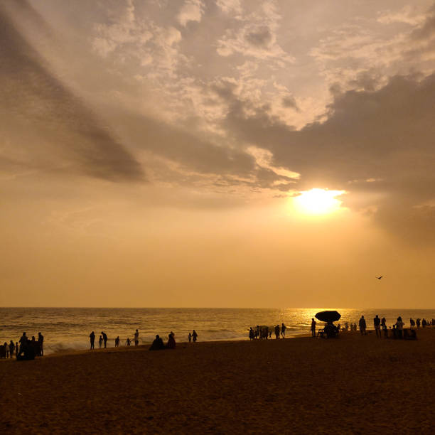 A silhouette landscape image of people watching sunset on a beach in Kerala, India.