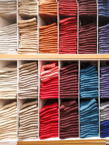 Shelves in a clothing store with T-shirts, T-shirts, socks, pantyhose, stockings folded in colors of the rainbow, shades of pink, black, gray, blue, yellow