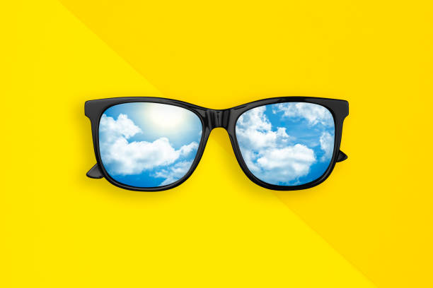 Sunglasses with reflection blue sky and cloud on yellow, orange background. Creative fashion minimal concept. Summer background. Flat lay. Top view