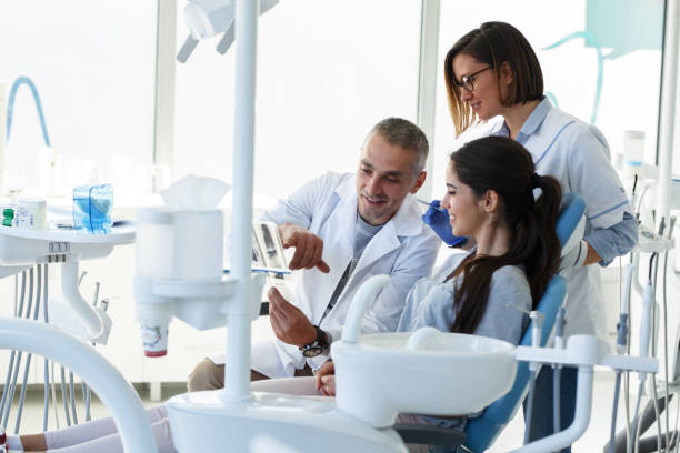 Dentist and his assistant in dental office talking with young female patient and preparing for treatment. stock photo