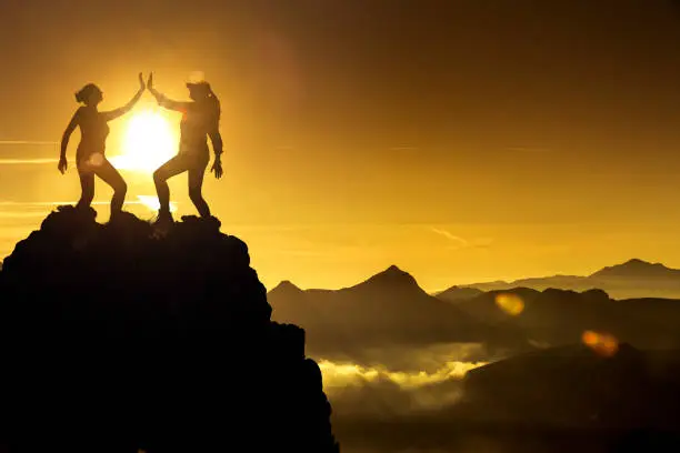 Two women high five on a mountaintop Silhouette