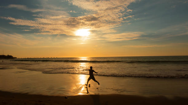 Silhouette of boys playing football against a warm sunrise sky.