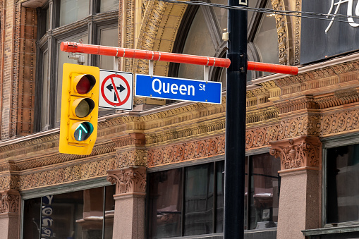 Toronto, Canada - March 04, 2019: Closeup sign of Queen St and traffic light with historic building in background in downtown Toronto Canada. Queen Street is a major east-west thoroughfare in Toronto.