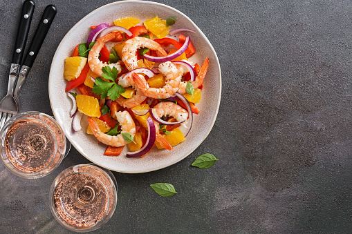 Ceviche with shrimps and orange, two glasses of pink sparkling wine, dark rustic background. Top view, copy space