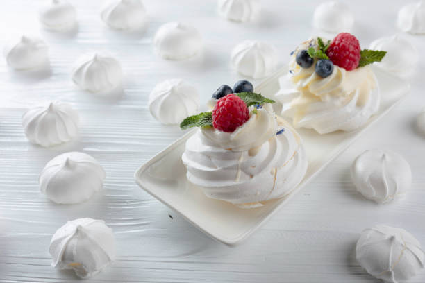 Meringues with fresh berries of raspberry, blueberry and red currant. The dessert is decorated with mint leaves. Light background. Close-up. Macro shooting.