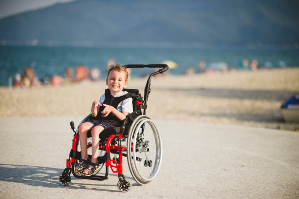 Smiling young boy on the wheelchair by the sea stock photo