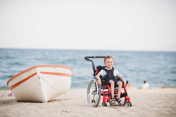 Cute young boy on the wheelchair by the sea Smiling young boy on the wheelchair by the sea atrophy photos stock pictures, royalty-free photos & images