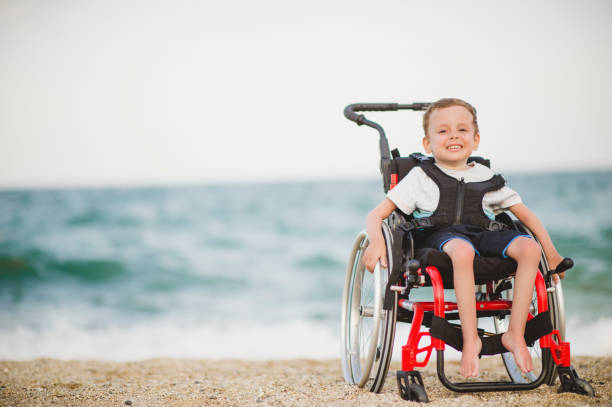 Smiling young boy on the wheelchair by the sea stock photo
