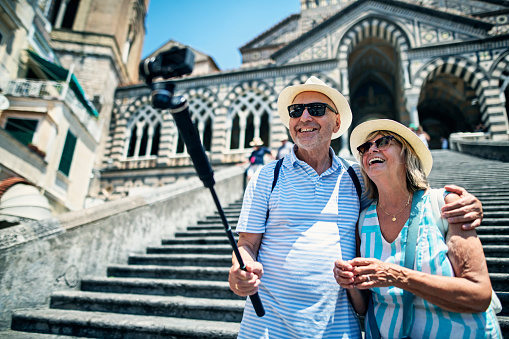 Happy senior couple sightseeing Amalfi, filming themselves with modern camera