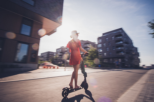 Young woman riding electric scooter at sunny day.