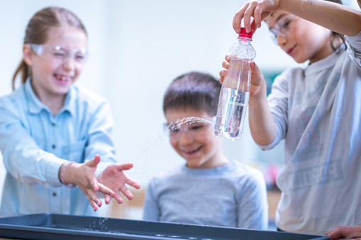 Elementary schoolgirl and two schoolboys doing science experiment on a chemistry class.