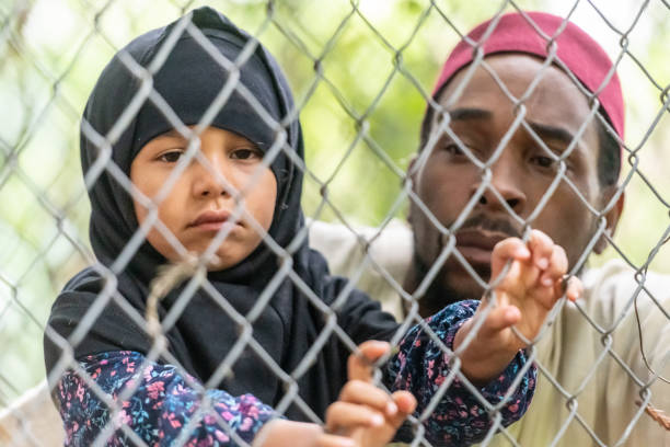 мусульманский середине взрослого черного человека, держащего свою дочь, глядя через забор - kufi стоковые фото и изображения