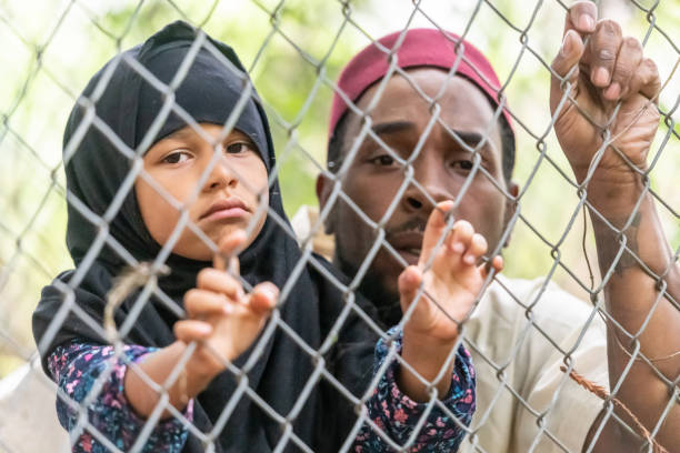 Muslim mid adult black man holding his daughter looking through a fence Muslim mid adult refugee black man holding his daughter looking through a fence trying to emigrate to a better future running away from war and violence refugee camp stock pictures, royalty-free photos & images