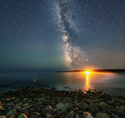 The Summer Milky Way and a distant campfire illuminate a beach.  Long exposure.