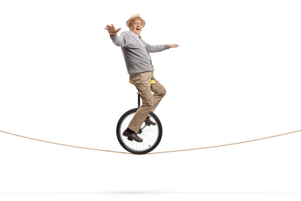 istock Elderly man riding a unicycle on a rope and balancing with hands 1164427150